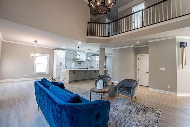 living area featuring baseboards, a chandelier, light wood-style flooring, and crown molding