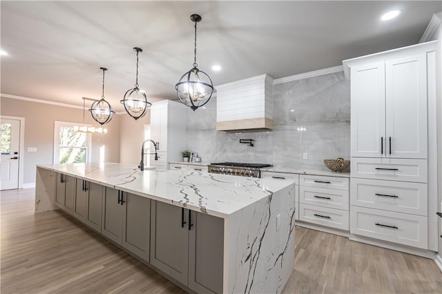 kitchen with a large island, tasteful backsplash, ornamental molding, light wood-style floors, and premium range hood