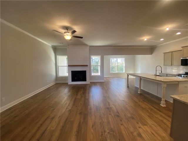 unfurnished living room featuring a fireplace, sink, dark hardwood / wood-style flooring, ornamental molding, and ceiling fan