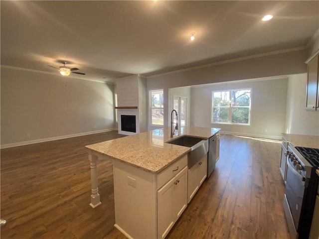 kitchen with appliances with stainless steel finishes, a kitchen island with sink, a fireplace, light stone countertops, and white cabinets