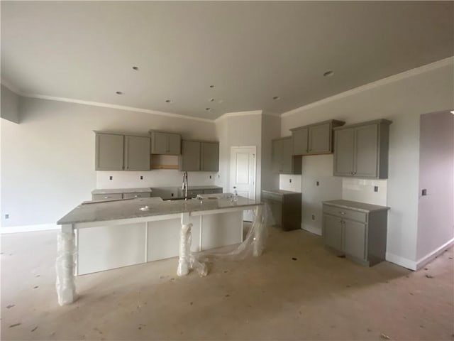 kitchen featuring gray cabinets, an island with sink, sink, a kitchen bar, and ornamental molding