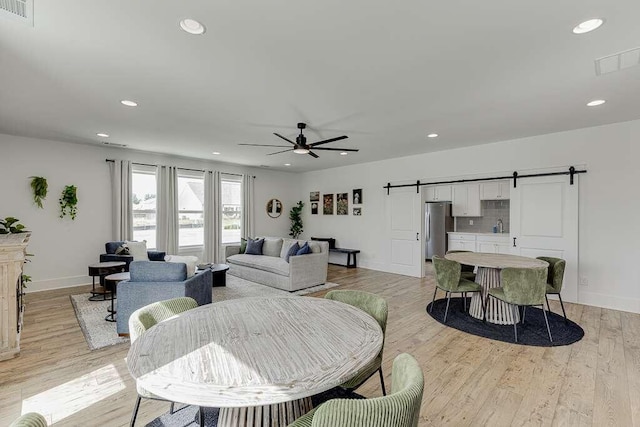 living room featuring ceiling fan, a barn door, sink, and light wood-type flooring