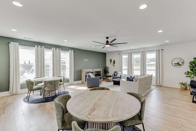 dining room with a fireplace, ceiling fan, and light wood-type flooring