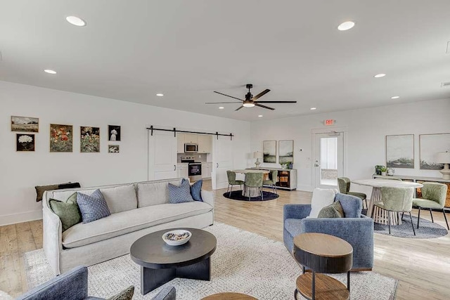 living room with ceiling fan, a barn door, and light wood-type flooring