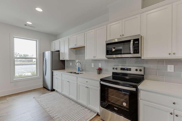 kitchen with sink, light hardwood / wood-style flooring, appliances with stainless steel finishes, tasteful backsplash, and white cabinets