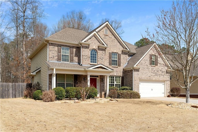 traditional-style house featuring fence, an attached garage, a shingled roof, concrete driveway, and brick siding