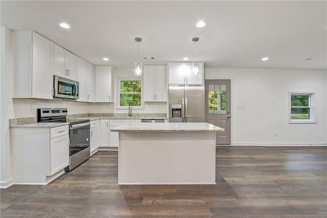 kitchen with light stone countertops, white cabinetry, a center island, hanging light fixtures, and stainless steel appliances