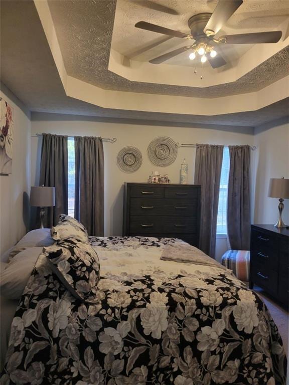 bedroom with ceiling fan, a tray ceiling, and a textured ceiling