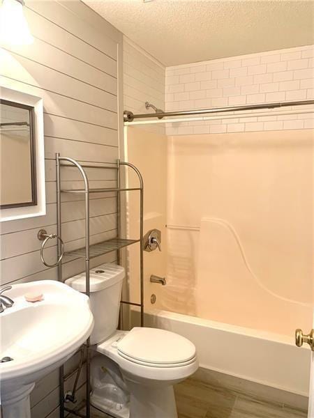 full bathroom featuring toilet, wood-type flooring, sink, tiled shower / bath, and a textured ceiling