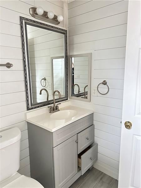 bathroom featuring wooden walls, hardwood / wood-style floors, vanity, and toilet