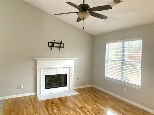 unfurnished living room featuring lofted ceiling, wood-type flooring, a tile fireplace, and ceiling fan