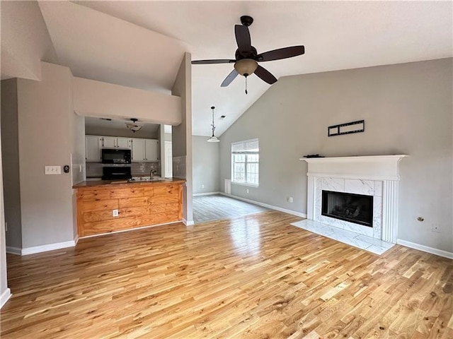 unfurnished living room with sink, a premium fireplace, light wood-type flooring, and ceiling fan