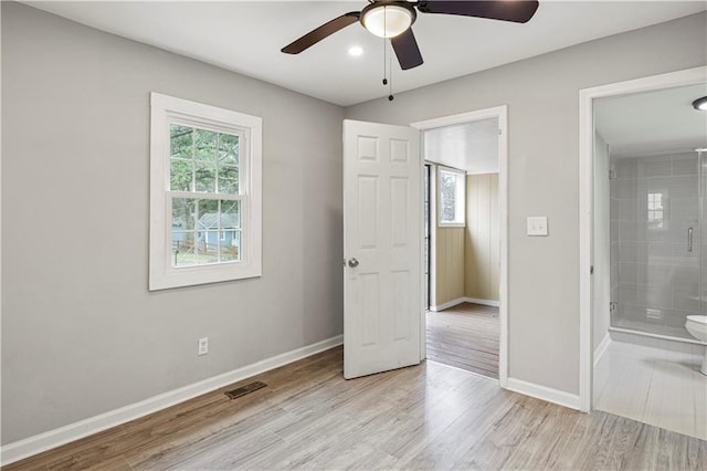 unfurnished bedroom featuring multiple windows, ensuite bath, light wood-type flooring, and ceiling fan