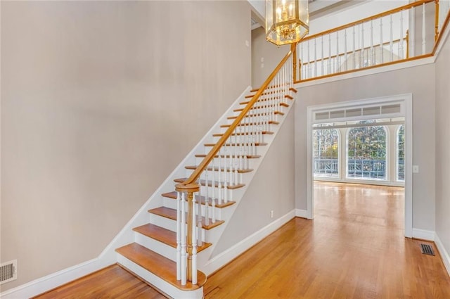 staircase featuring wood-type flooring, a towering ceiling, and a chandelier