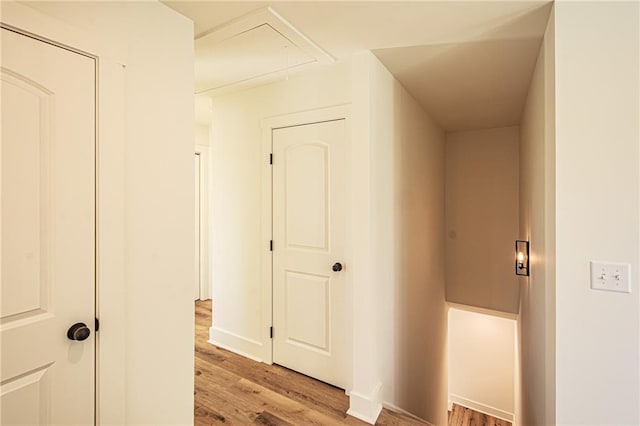 hall featuring light wood-style floors, attic access, and baseboards