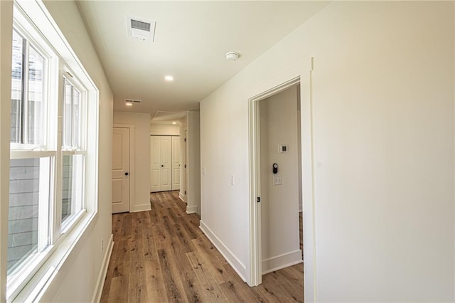 corridor with light wood-type flooring, visible vents, and baseboards