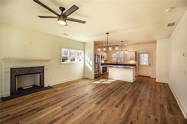 unfurnished living room with dark wood-type flooring, a fireplace with flush hearth, visible vents, and baseboards