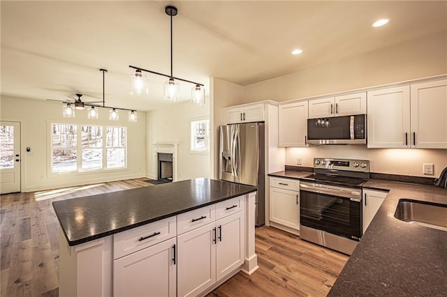 kitchen featuring plenty of natural light, dark countertops, stainless steel appliances, a fireplace, and a sink