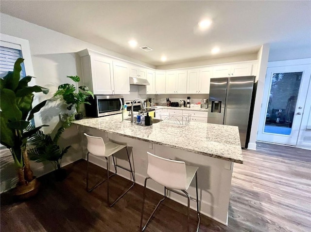 kitchen with a kitchen bar, light stone countertops, stainless steel appliances, sink, and white cabinets