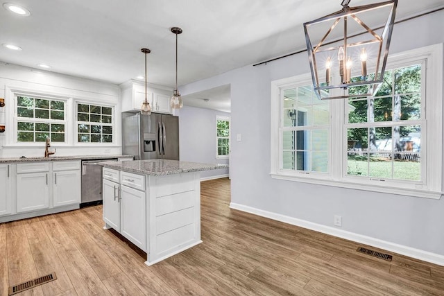 kitchen featuring stainless steel appliances, a kitchen island, hanging light fixtures, and white cabinets