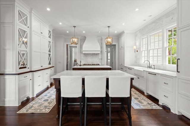 6440 Westchester Pl, Cumming, GA 30040 - kitchen with premium range hood, a kitchen island, ornamental molding, white cabinetry, and a kitchen breakfast bar