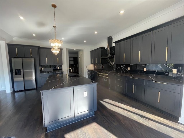 kitchen with pendant lighting, a kitchen island with sink, backsplash, stainless steel fridge with ice dispenser, and wall chimney exhaust hood