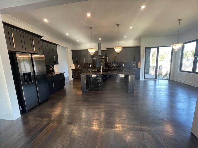 kitchen featuring stainless steel refrigerator with ice dispenser, an inviting chandelier, decorative light fixtures, ventilation hood, and an island with sink