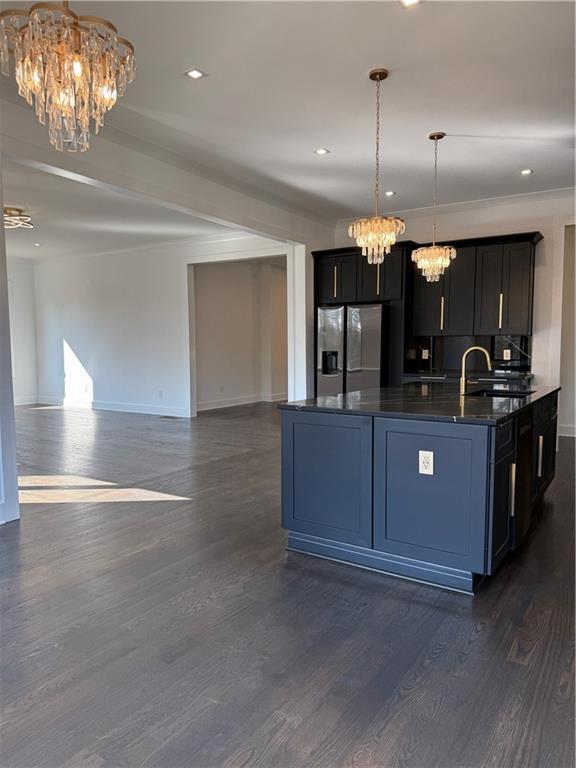 kitchen with pendant lighting, stainless steel fridge with ice dispenser, a notable chandelier, and an island with sink