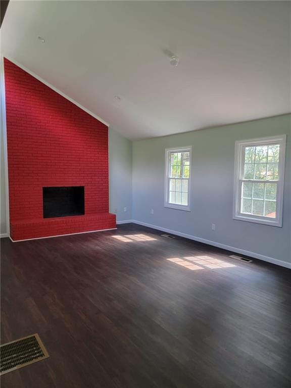 unfurnished living room with lofted ceiling, a healthy amount of sunlight, dark wood-type flooring, and a brick fireplace