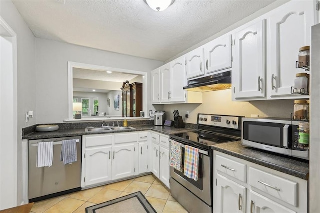kitchen with dark countertops, under cabinet range hood, white cabinets, a sink, and appliances with stainless steel finishes