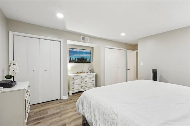 bedroom featuring two closets, recessed lighting, light wood-style flooring, and visible vents