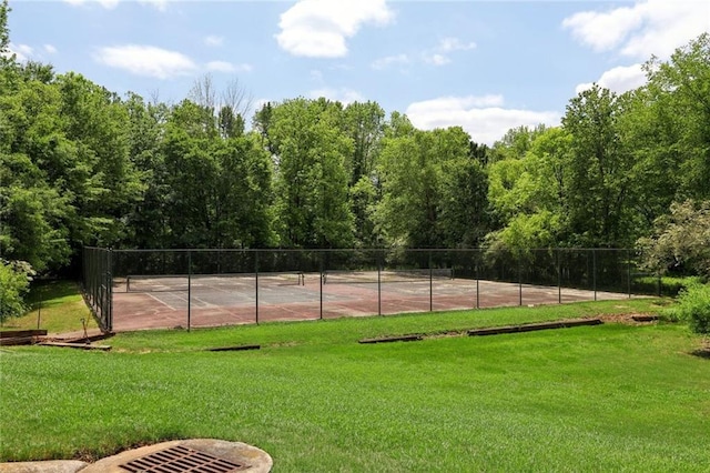 view of tennis court featuring a lawn and fence