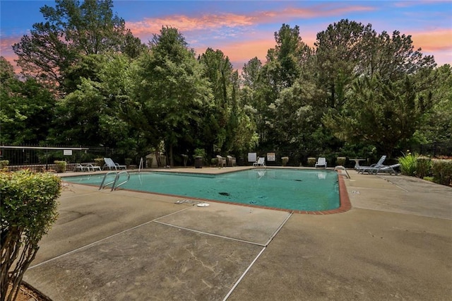 pool at dusk with fence, a patio, and a community pool