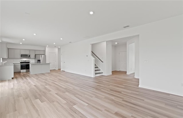 unfurnished living room with recessed lighting, visible vents, stairway, and light wood finished floors