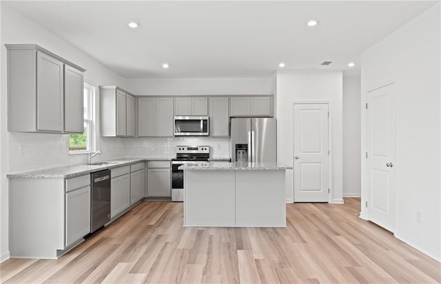 kitchen featuring gray cabinetry, stainless steel appliances, a center island, light wood-style floors, and decorative backsplash