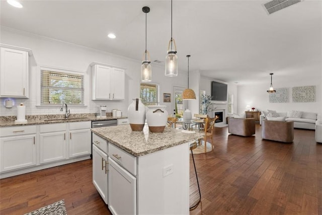 kitchen with sink, white cabinetry, light stone counters, decorative light fixtures, and a kitchen island