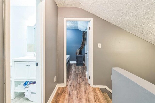 504 J C Daniel Rd, Carrollton, GA 30117 - hallway featuring a textured ceiling, vaulted ceiling, light wood-style flooring, baseboards, and a sink