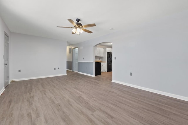 unfurnished living room featuring ceiling fan, arched walkways, light wood-style flooring, and baseboards