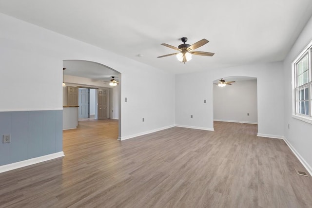 unfurnished living room with a ceiling fan, arched walkways, visible vents, and light wood finished floors