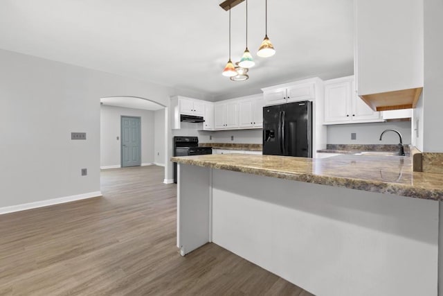 kitchen featuring arched walkways, a sink, a peninsula, under cabinet range hood, and black appliances