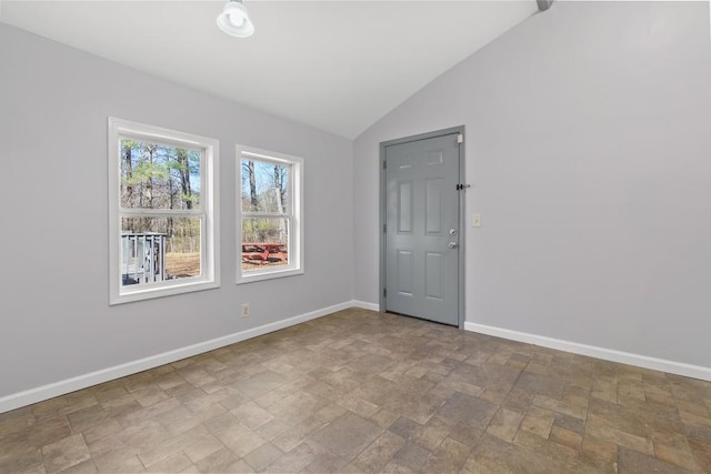 empty room featuring stone finish floor, vaulted ceiling, and baseboards