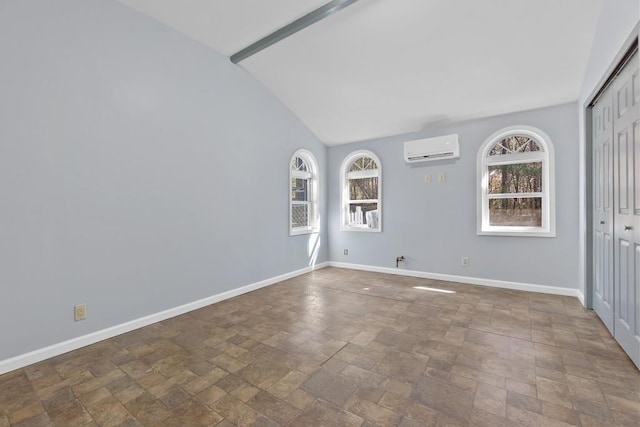 spare room featuring a healthy amount of sunlight, a wall mounted air conditioner, stone finish floor, and baseboards