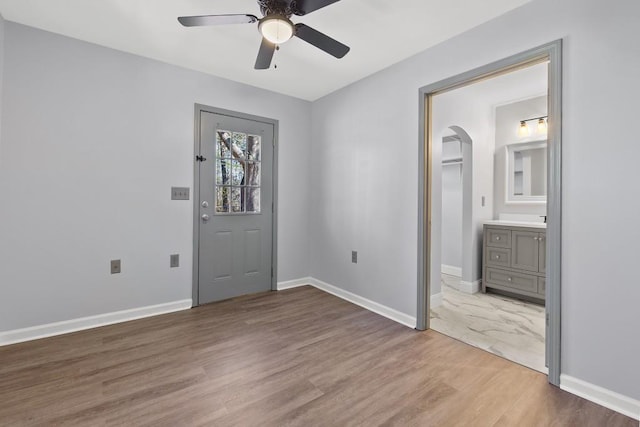 entryway featuring ceiling fan, baseboards, arched walkways, and wood finished floors