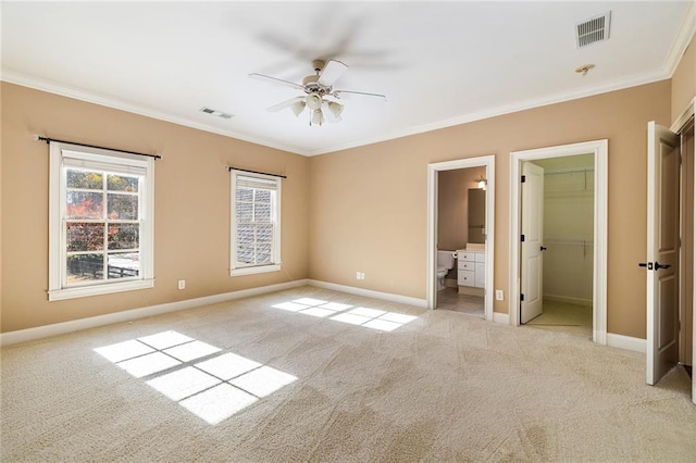 unfurnished bedroom with light carpet, ensuite bath, ceiling fan, a spacious closet, and ornamental molding