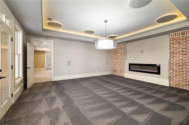 unfurnished living room with dark carpet, brick wall, and a tray ceiling