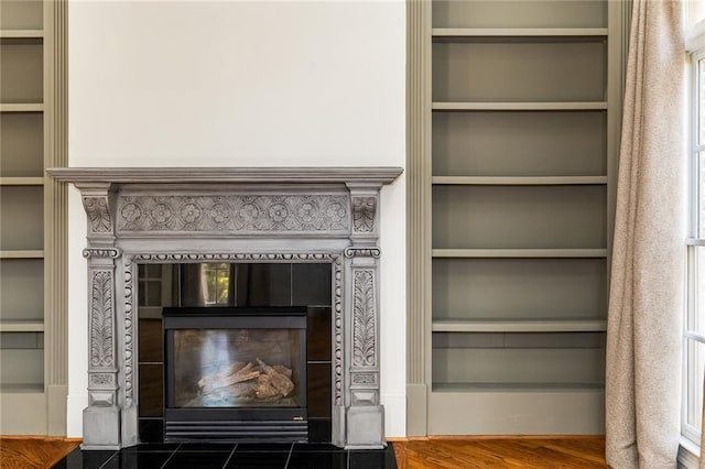 interior details featuring hardwood / wood-style floors, built in features, and a tiled fireplace