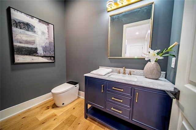 half bath with vanity, toilet, wood finished floors, and baseboards