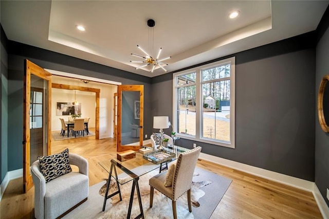 dining area featuring an inviting chandelier, a raised ceiling, baseboards, and wood finished floors