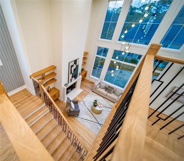 staircase featuring wood finished floors, baseboards, a towering ceiling, and a healthy amount of sunlight