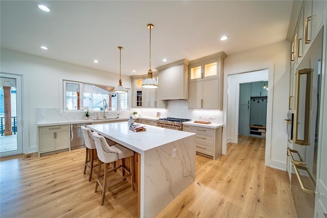 kitchen featuring light wood finished floors, tasteful backsplash, a kitchen island, stainless steel appliances, and a sink